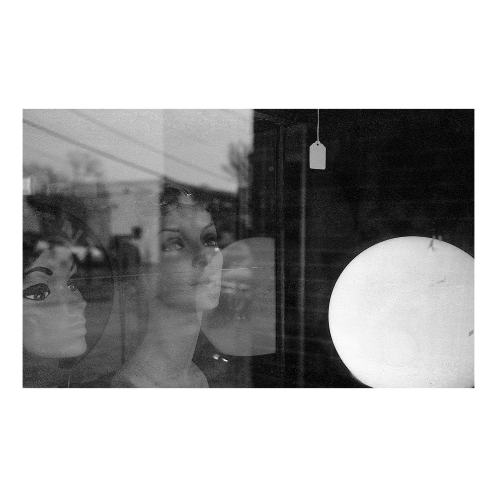 Two mannequin heads are illuminated by a nearby lamp through the window of an antique shop. 