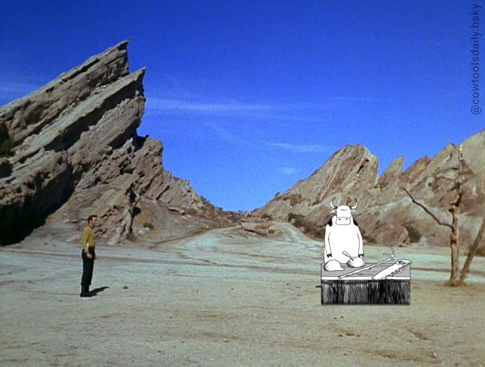 Edited Star Trek TOS screenshot. 

in a desert scene, with jagged rock formations in the background, Captain James T Kirk squares off with a bipedal cow who is standing behind a table with 4 crudely made tools on it.