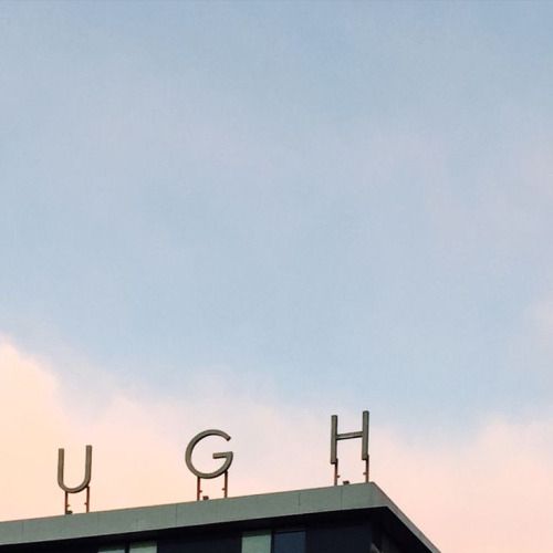the letters "U", "G", and "H" as apart of a rooftop sign, framed to spell UGH along the bottom of the photo with the upper two thirds of the fame being a gentle soft blue sky with slight cloud cover. 