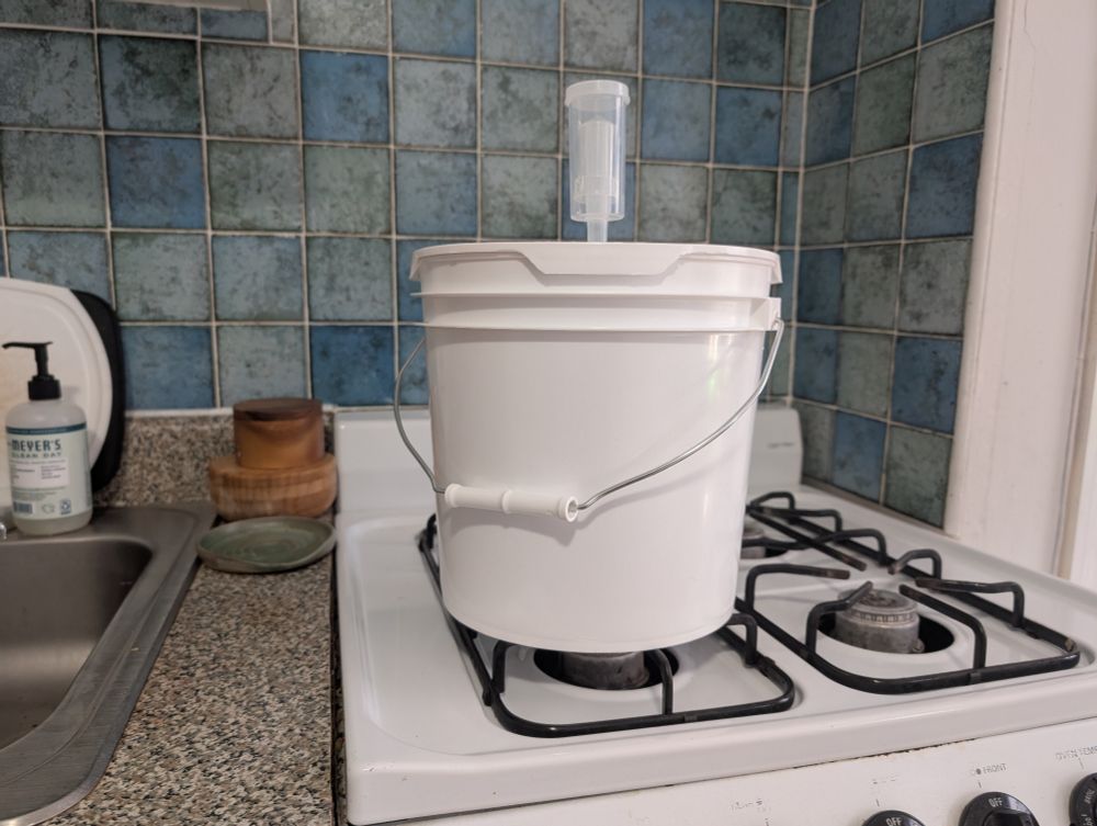 A white gallon bucket with a little plastic vent on top sitting on a stove top