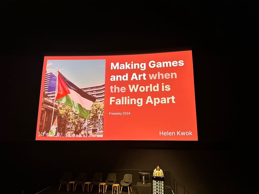 Helen stands below a slide featuring the Palestinian flag at a pro-Palestine rally, along with the title of her talk: Making Games and Art when the World is Falling Apart