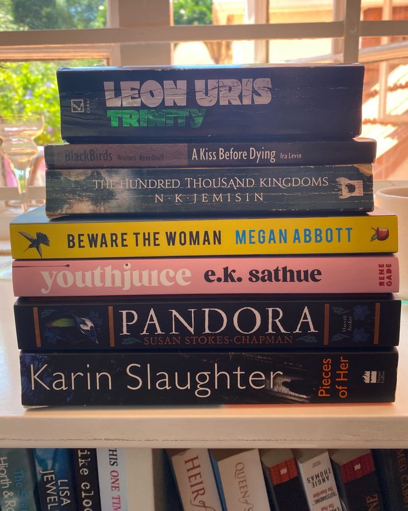 A pile of paperbacks (listed in the post) in a sunny patch on a white bookshelf. 