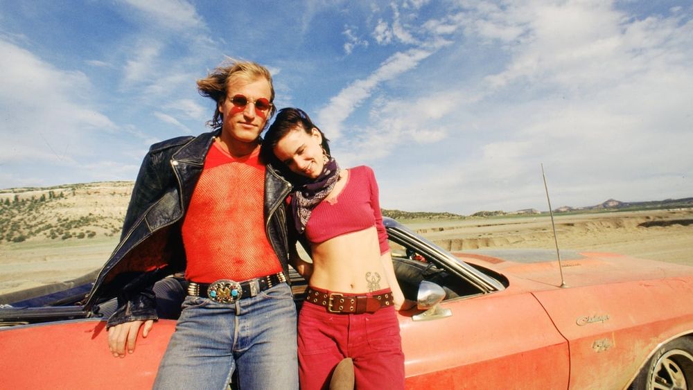 Woody Harrelson and Juliette Lewis in a promo shot from Natural Born Killers, they're posed leaning against a red convertible car, and Woody is wearing a red mesh top that was probably too much to expose good catholic Irish ladies to