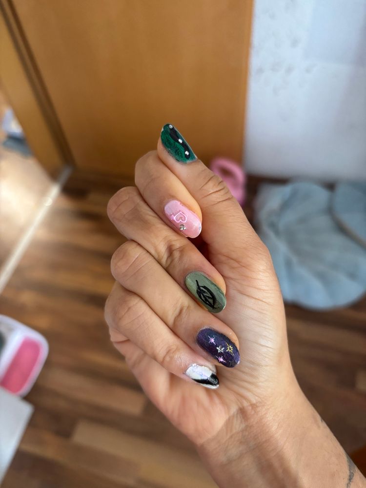 picture of a hand showcasinh nail art. each finger is different. the thumb is a sparkly green with a black wiggly line that’s supposed to be a snake and some rhinestones. index is a soft pink with hearts. middle a sage metallic green with a pointed on leaf. ring a sparkly purple with pink and gold stars. pinky is a shimmery white with a black diagonal line
