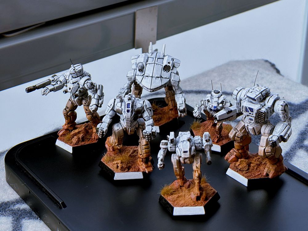 Six miniature battlemechs painted in stark white, on a dusty red base. 