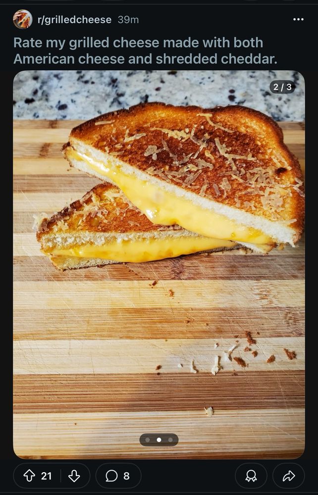 Grilled cheese sandwich on a cutting board, cut diagonally, with some of the cheddar oozing out. 