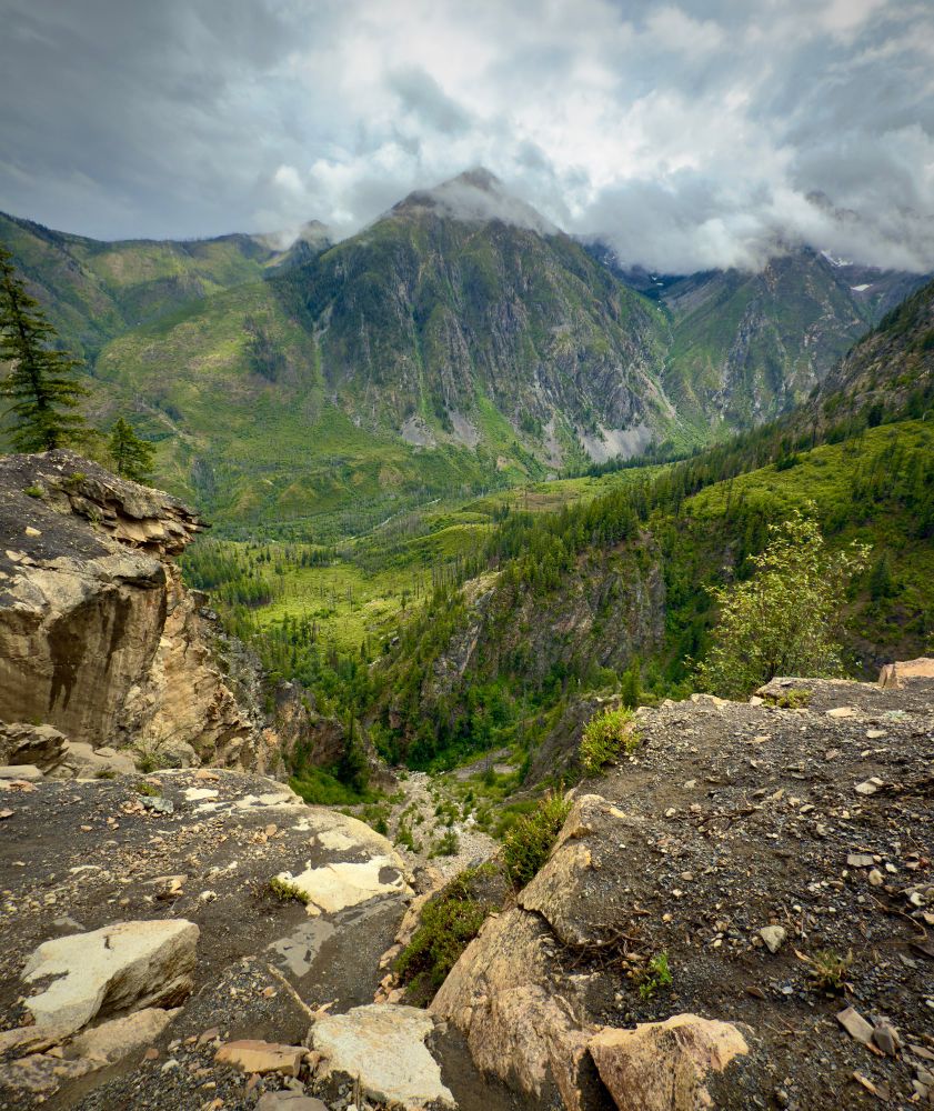 Mountain with clouds in the distance, looking over a cliff side to a river below