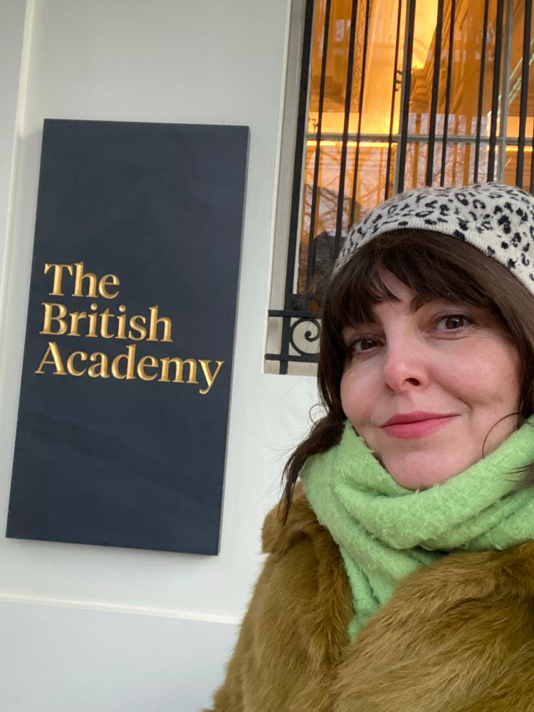 A white woman standing next to a sign saying the British academy 