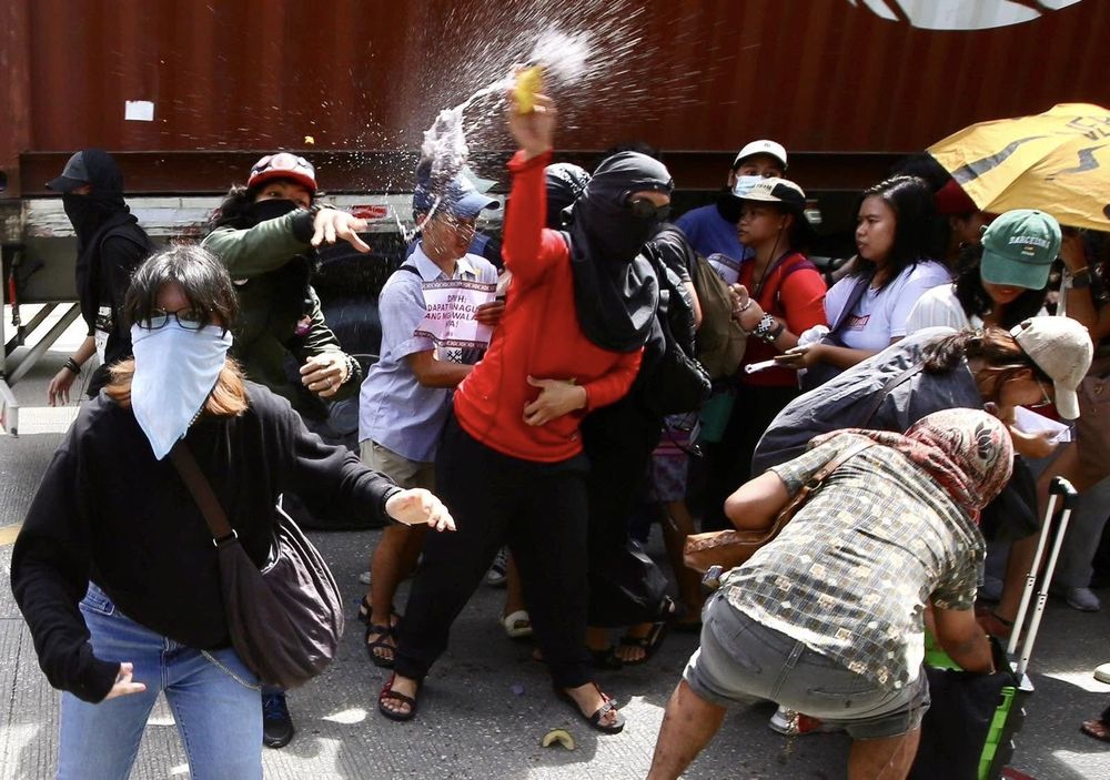 Militants in hoods and masks throw garbage at police (who are out of the frame)