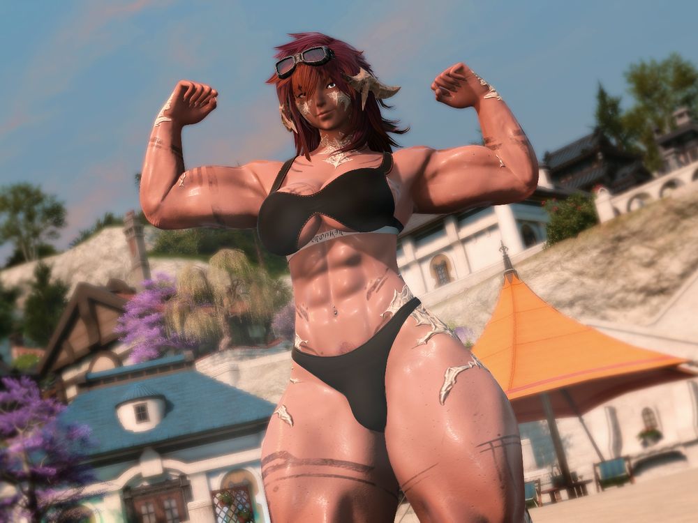 Aro on a beachfront in a sports bra and underwear. She is stood flexing both her arms showing off her muscles.