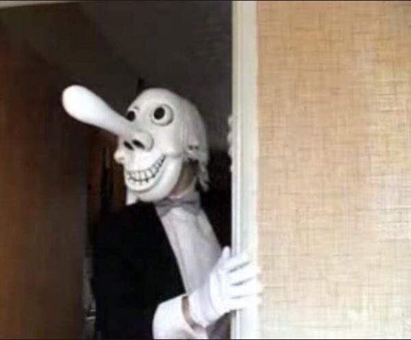 Mr. Noseybonk, with long dong like nose, and white gloves, bow tie and black dinner jacket looking towards something whilst stood in a doorframe