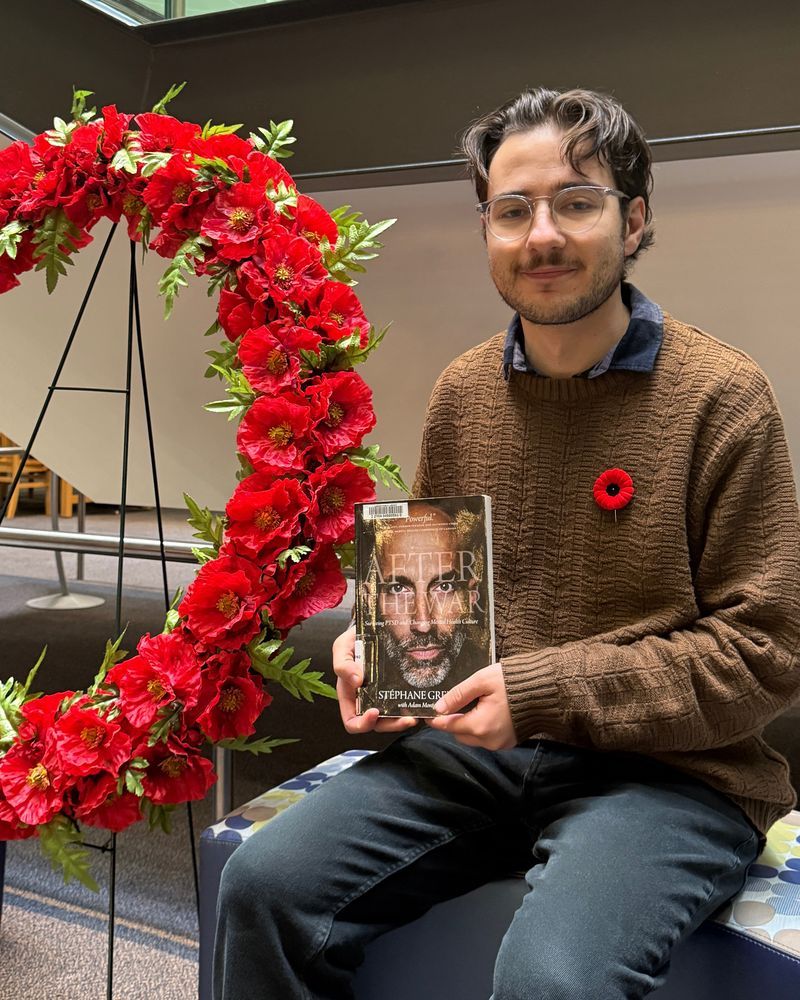 A staff member holds the book After the war : surviving PTSD and changing mental health culture by Stéphane Grenier, sitting next to a poppy garland. 