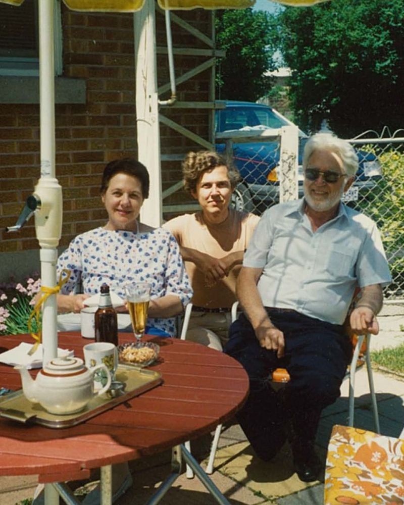 Rudy Sparkuhl and his parents sit outside at a patio table, squinting in the sun.