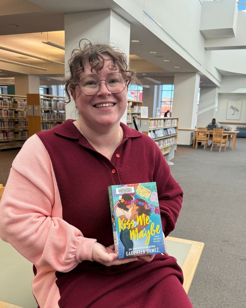 A staff member holding the book Kiss Me, Maybe
Gabriella Gamez