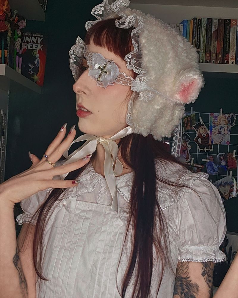 foto minha de perfil, com roupa branca, cheia de babados, touca de carneirinho e tapa olho de renda.