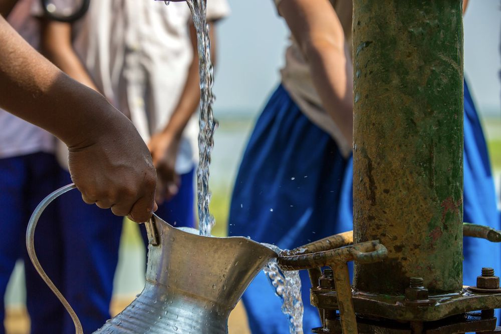 Stream of well water pouring into a metal pitcher. Credit: Lingkon Serao
