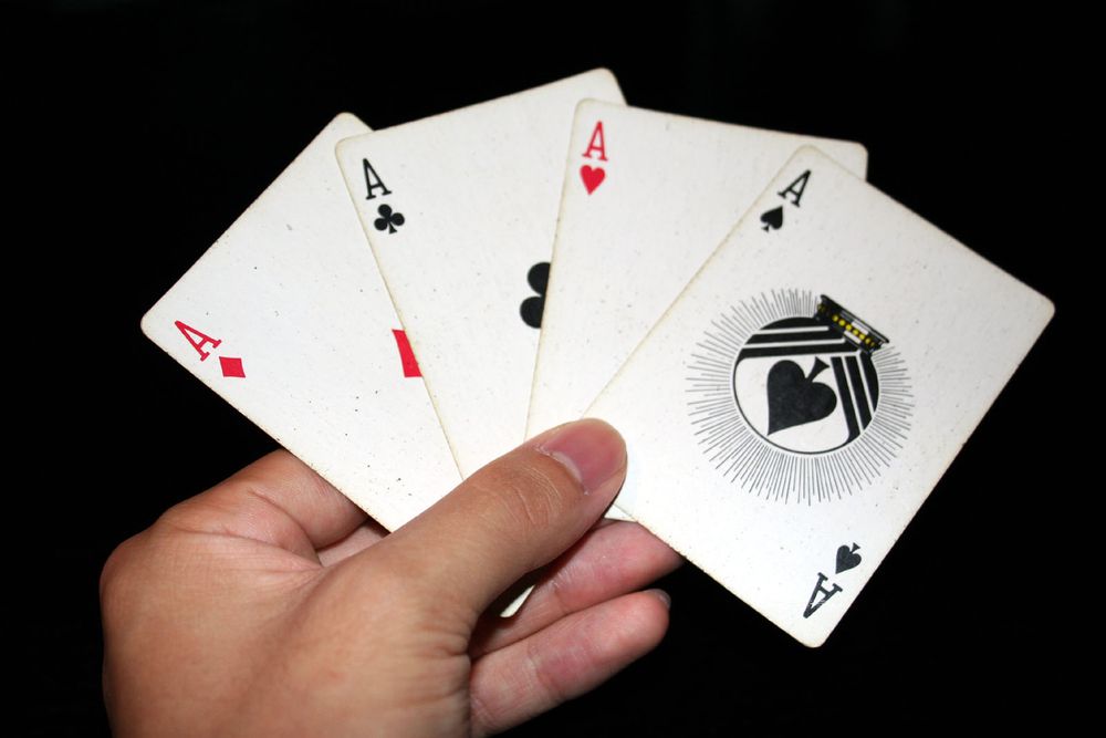 a hand holding four aces, one from each suit 