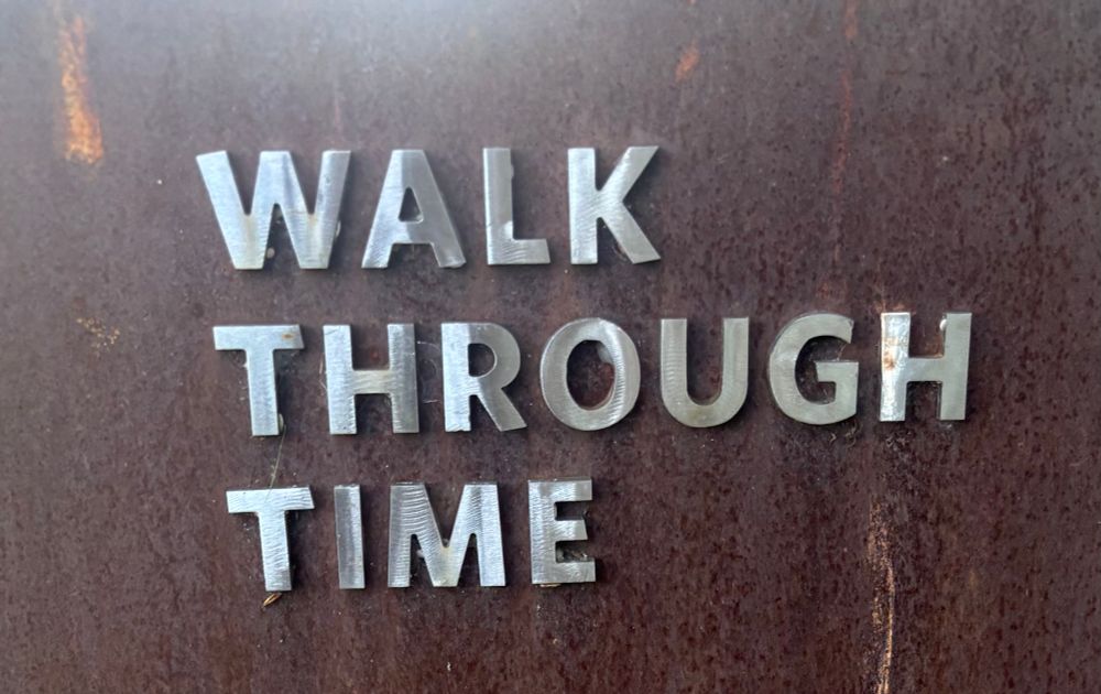 Metallic letters on wood-toned background; letters spell out “walk through time.”