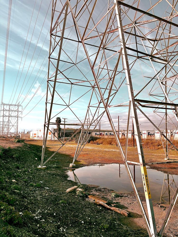 A small body of water under an electrical tower. 