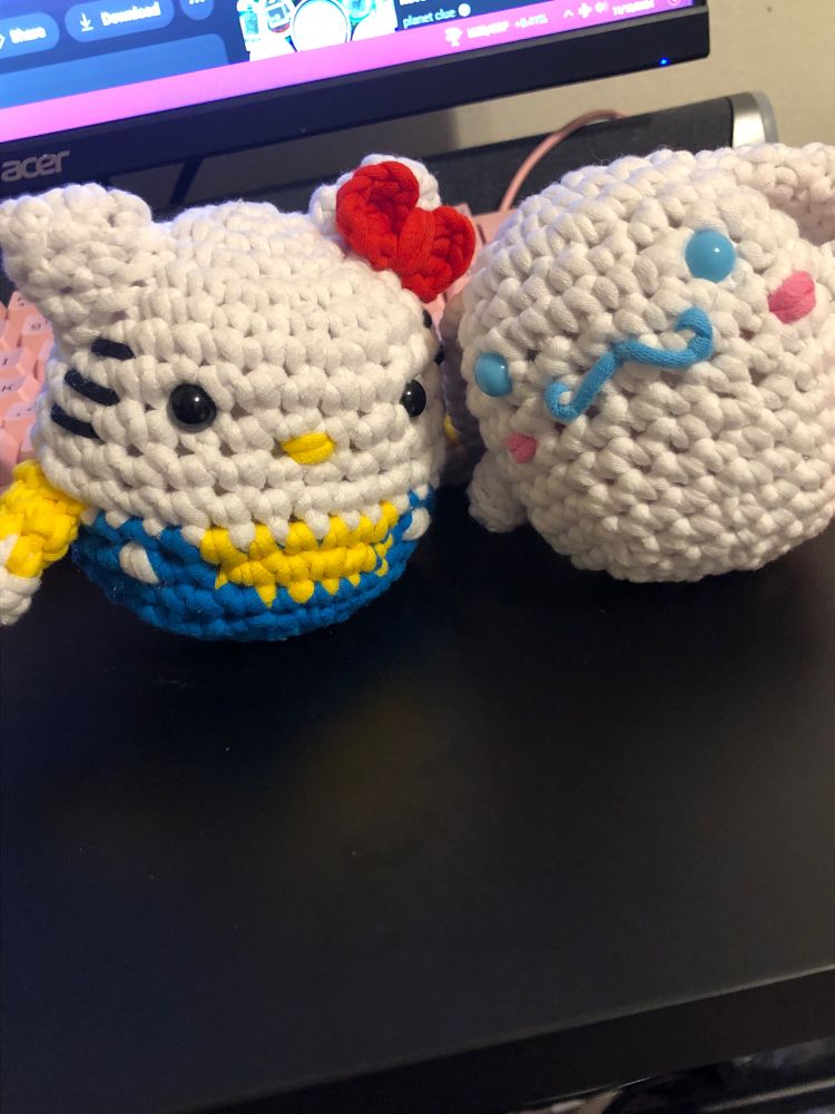 Siting on a desk is two crocheted peices from Sanrio. On the left is hello kitty and the right cinnamonroll. 