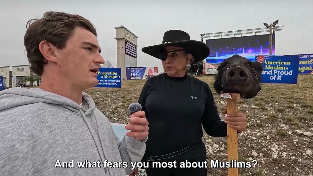 A guy and a hoodie asking "and what fears you most about Muslims?" to a woman with an eyepatch, sadly nice Western hat, and a literal decapitated pig head on a pole, who is standing in front of a Muslim place of worship