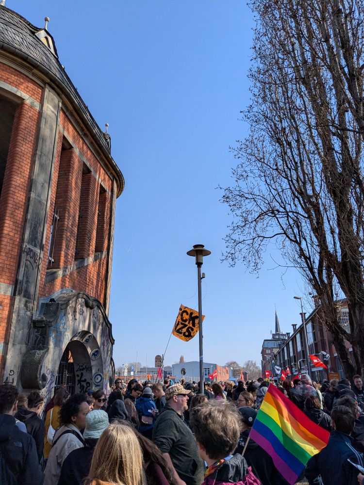 Gegenprotest Queermany, viele Menschen, Pride Flag und FCK NZS Fahne. 