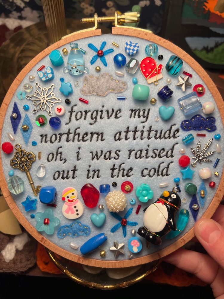charm embroidery of noah kahan’s song “northern attitude” in a blue color scheme