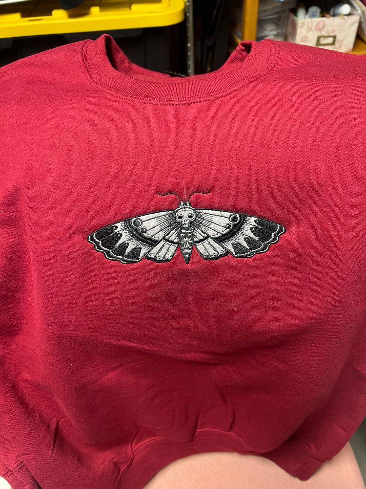 maroon crewneck sweatshirt with a black and white deathhead moth embroidered in the center
