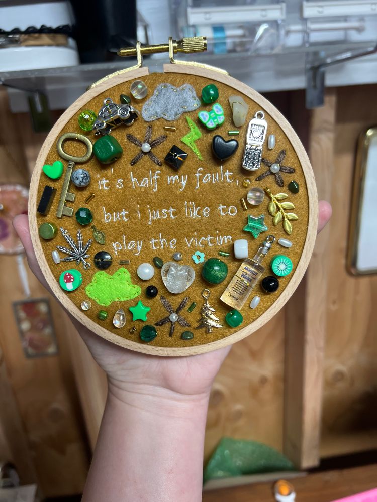 charm embroidery of noah kahan’s song “stick season” in a green/brown color scheme