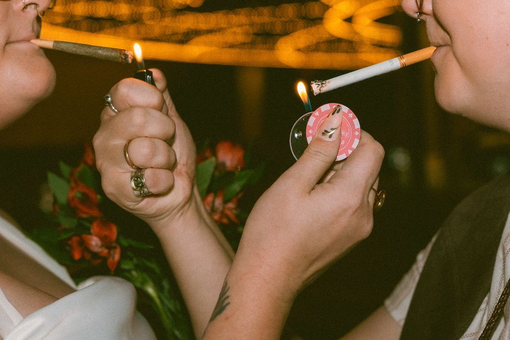 up close picture of noelle and joey lighting each other’s joint and cigarette. one of the lighters is a pink poker chip