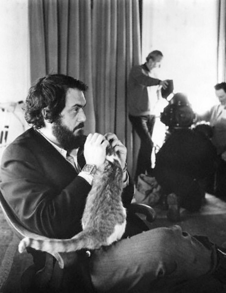 Black and white photo of Stanley Kubrick scratching the head of the cat in his lap.