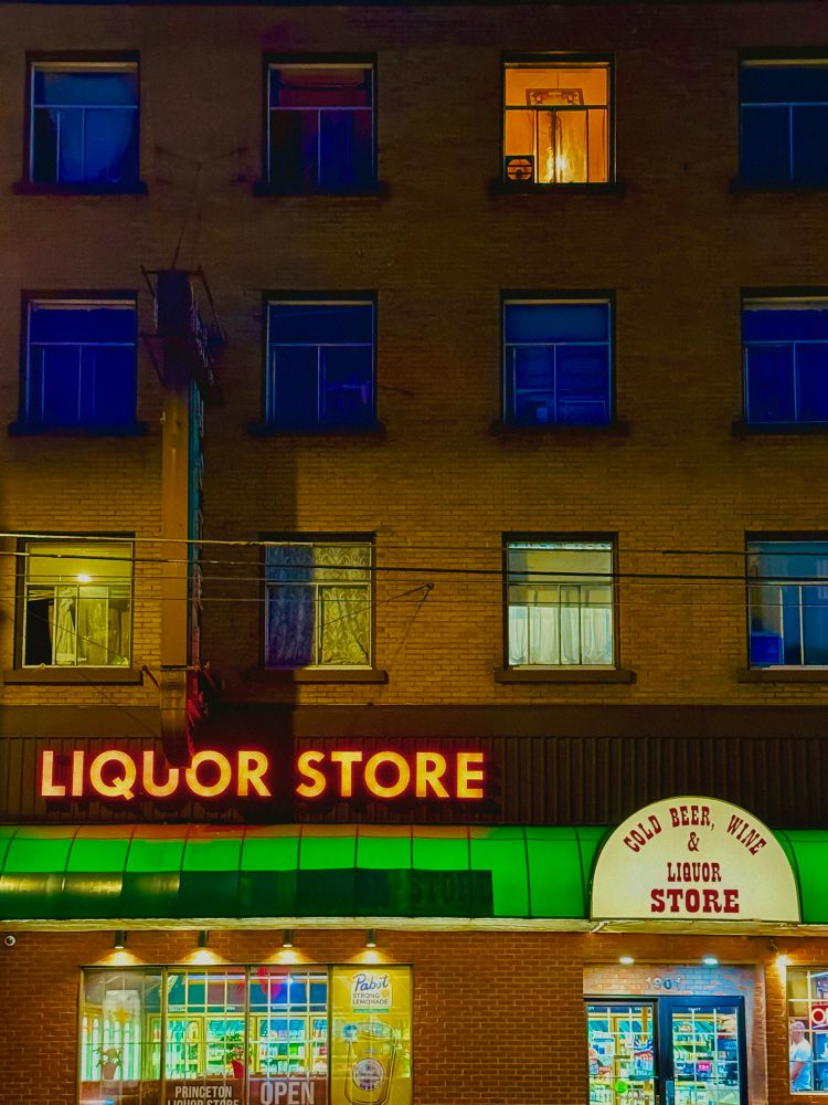 A lit up liquor store under an SRO with only a couple windows lit up, after dark. 
