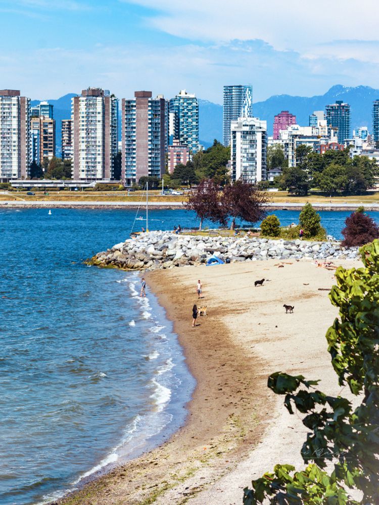 Sandy Vancouver beach shot from above, with skyscrapers and mountains in the background. 
