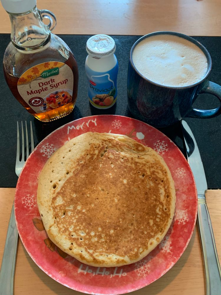 A plate with 2 American style pancakes, text on the top of the plate says “Merry”, text at the bottom of the plate says, “Ho,Ho,Ho!” 

There’s Dark Maple Syrup, a probiotic and a mug of fresh cappuccino… delicious breakfast! 🥞 ☕️ 🍁 