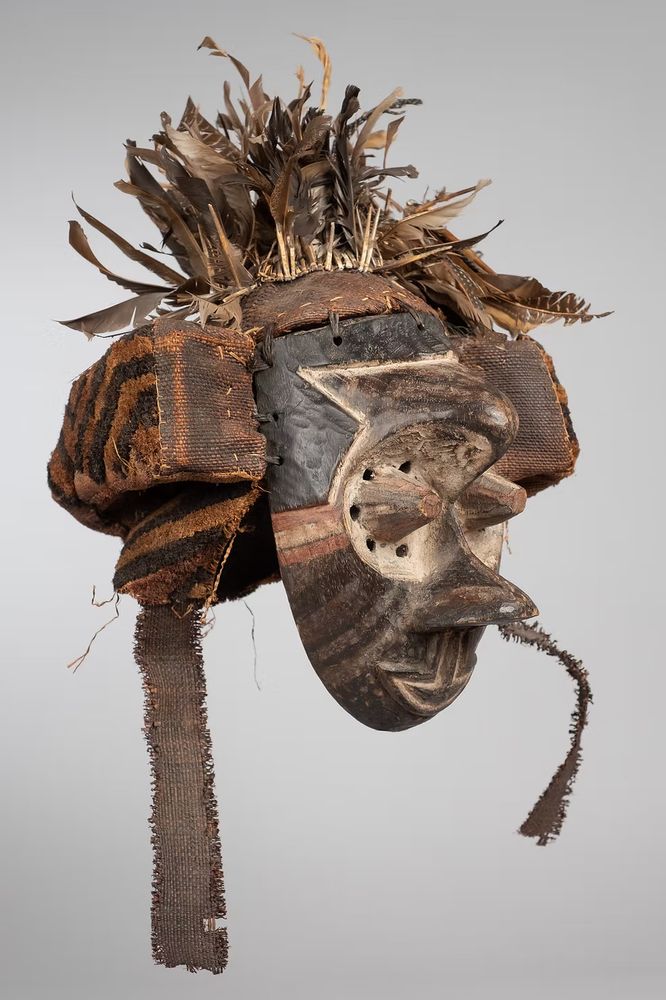 The Kuba Kingdom, also known as the Kingdom of the Bakuba or Bushongo, is a traditional kingdom in Central Africa. The Kuba Kingdom flourished between the 17th and 19th centuries in the region bordered by the Sankuru, Lulua, and Kasai rivers in the heart of the modern-day Democratic Republic of the Congo.
This mask may have represented a wise older man at boys’ initiations. One of the principal Kuba dance masks is called pwoom itok. The chief identifying characteristic is the shape of the eyes, whose centers are cones surrounded by holes through which the wearer sees. Like many Kuba types of masks, pwoom itok is extensively polychromed, or multicolored, and in this case adorned with many feathers at top.