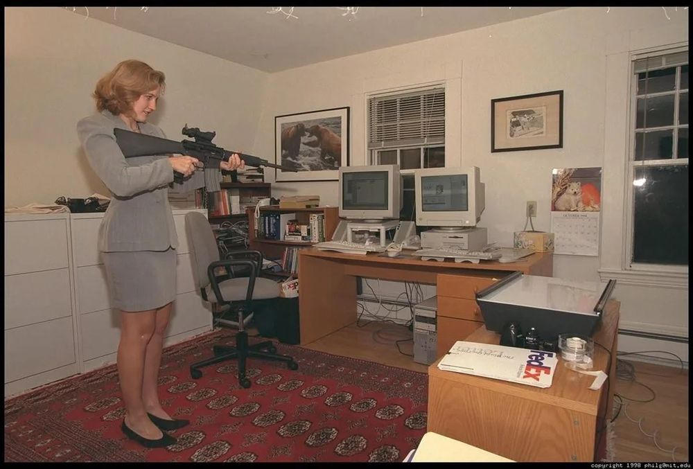 a woman pointing a rifle at a computer, with her finger on the trigger