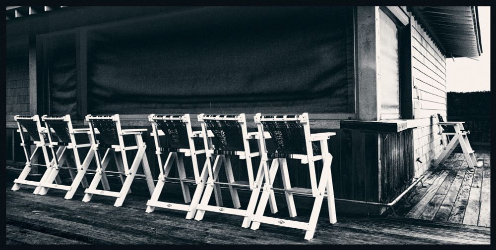 A winter scene at a summer beach resort. A row of tall bar chairs sit empty before a bar's serving counter. A heavy fabric screen covers the order window. It offers a quiet and lonely feeling compared to the bustle of summer.