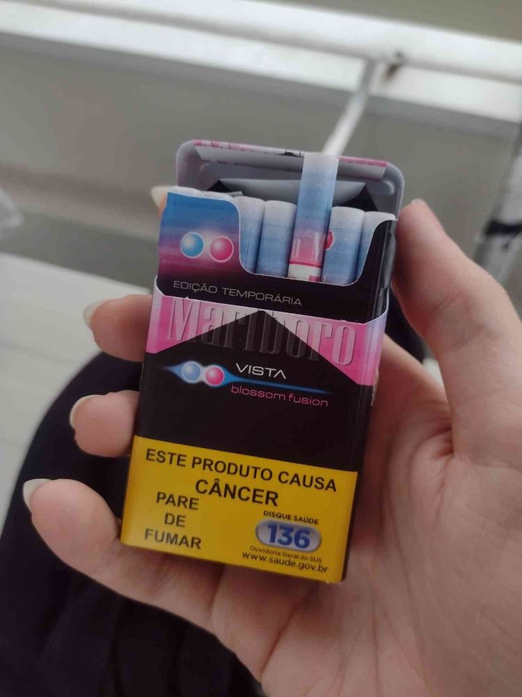 A hand holding an open pack of flavored Marlboro cigarettes, with the traditional red in the package design swapped for a gradient of white fused with blue and pink to indicate their two available flavours, tutti-frutti and menthol.