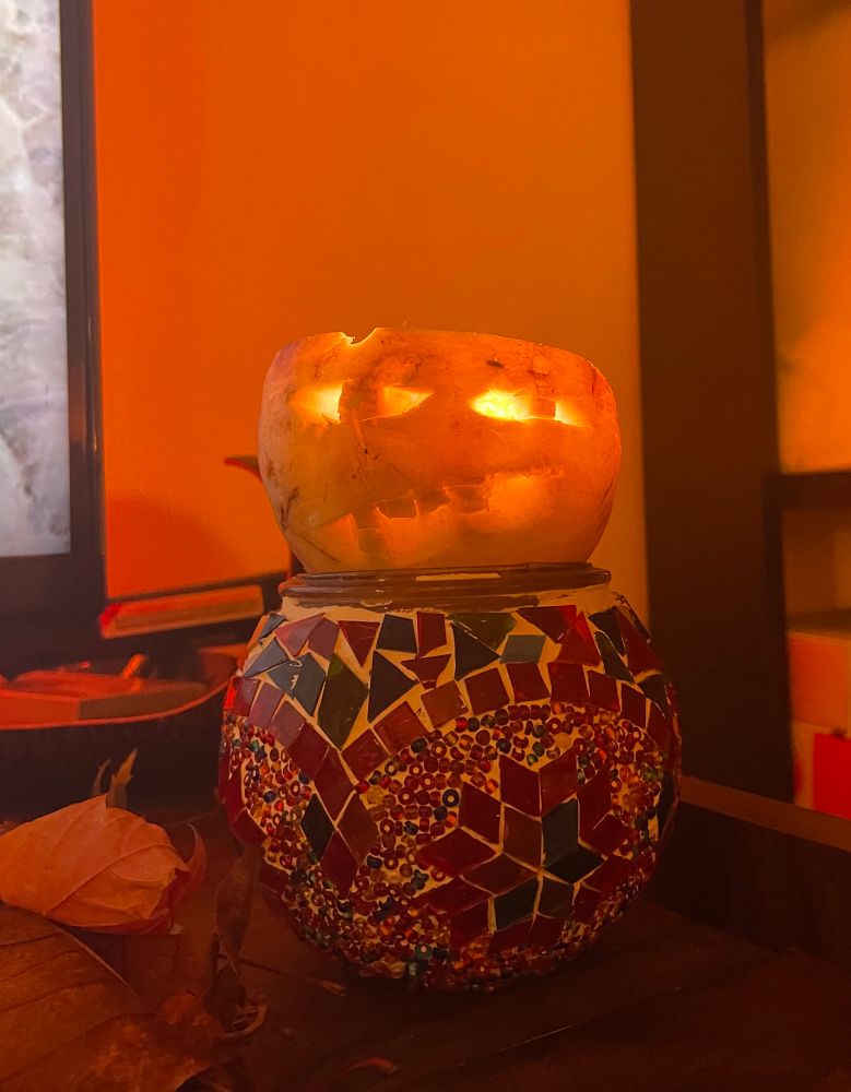 A roughly carved turnip, illuminated from a candle inside it, sitting on top a Turkish glass mosaic candle holder.