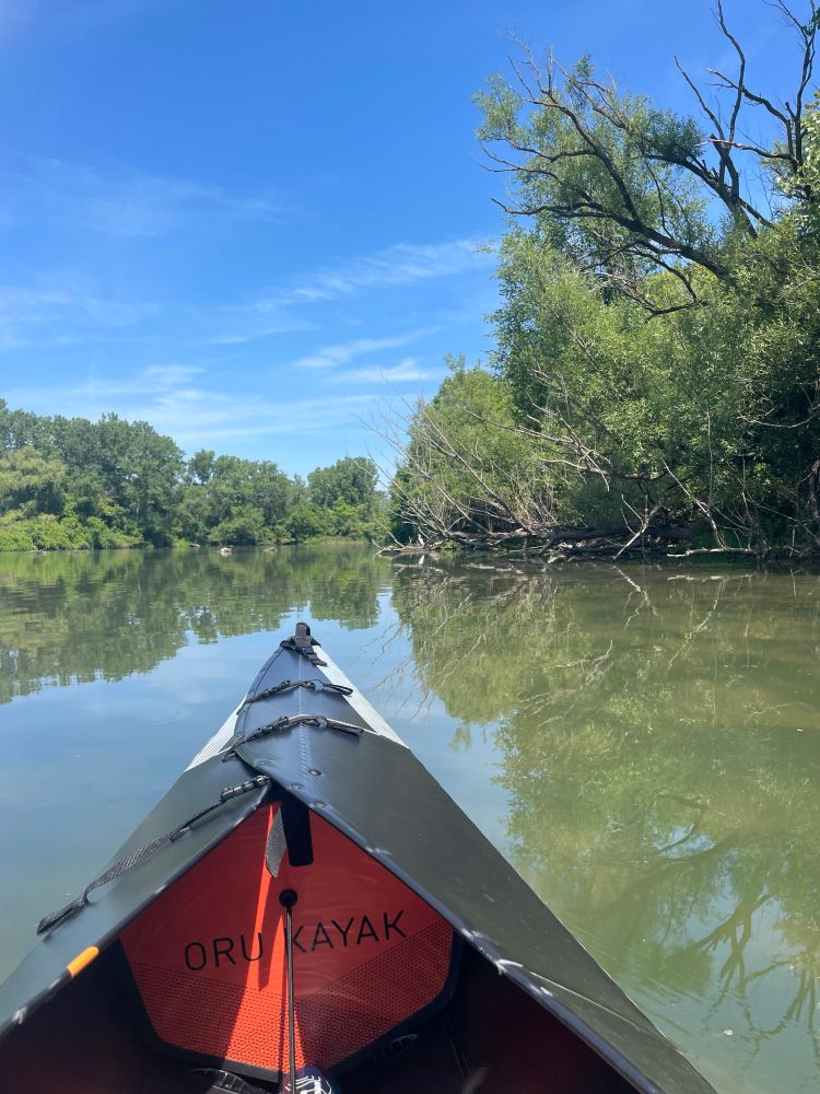 Foreground is a black and orange kayak on a wide calm river. In the background is a white egret on a log.