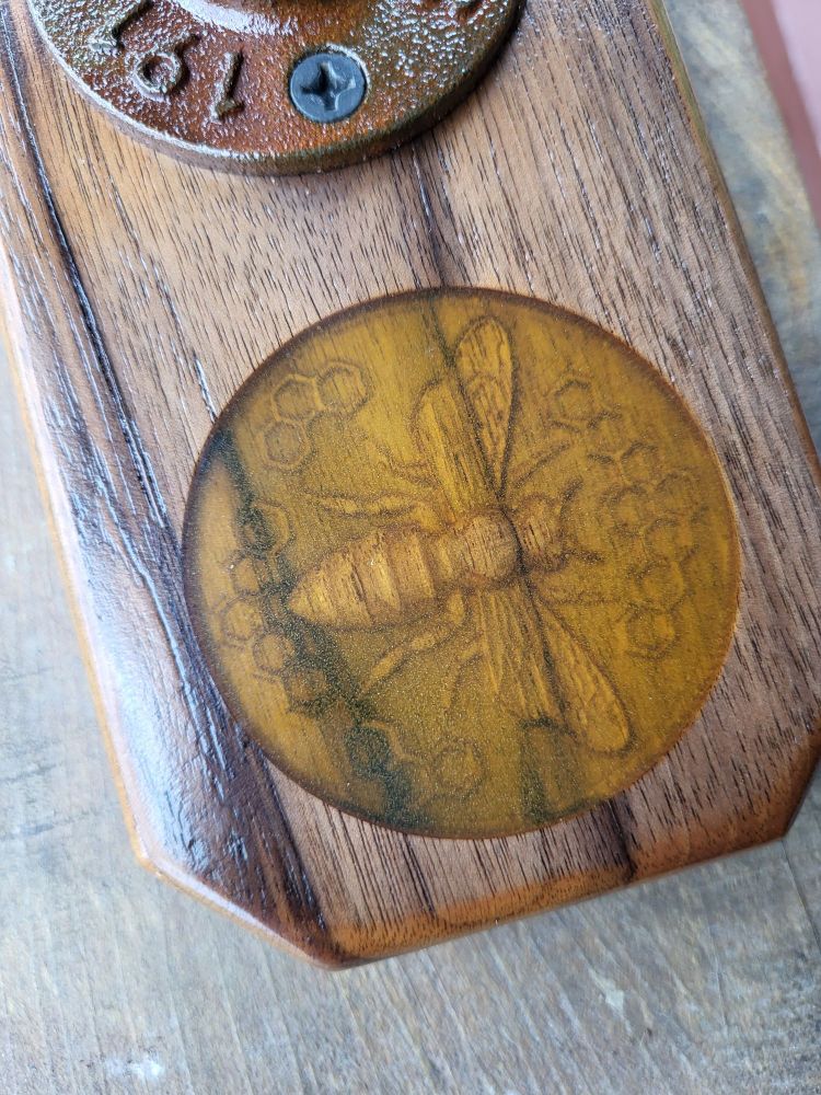 This close-up of the base shows the circular design of the bee carving and the yellow resin filling the space. The bee is seen from above and is nearly surrounded by honeycomb designs.