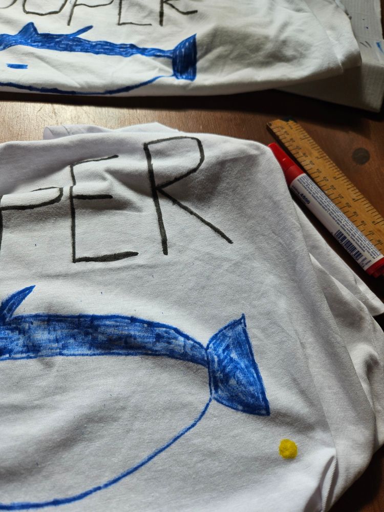 White tshirts on a table with mayhaps a fish drawn in blue on them 