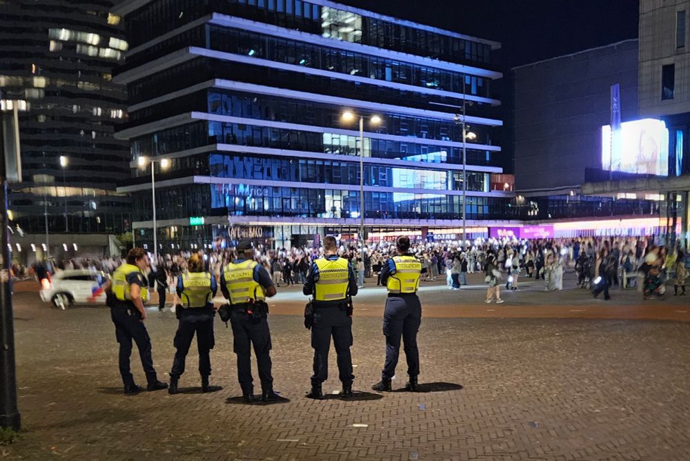 Five police officers watching a large crowd waving ARMY bombs