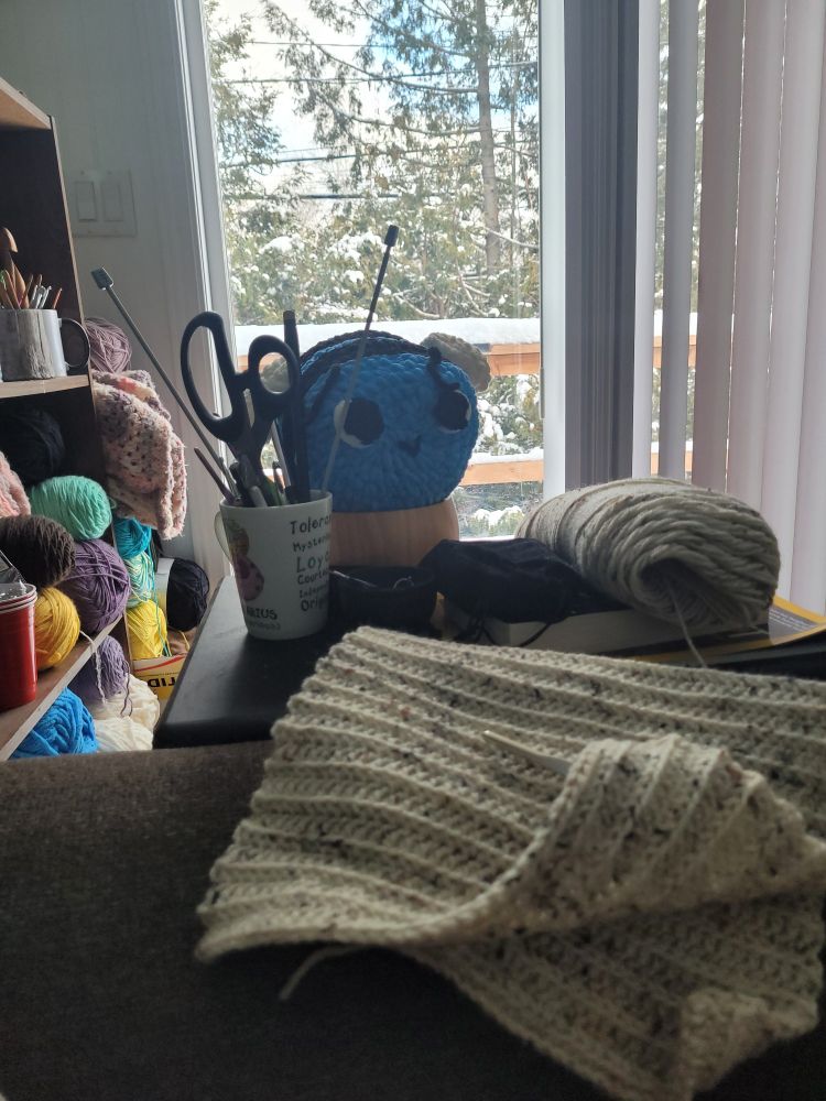 Beside me is an end table full of yarn. A work in progress hat and a finished plushie of a bee sits there.