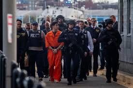 Luigi mangione walking handcuffed in orange while a huge, cluster fuck of armed, armored police walk surrounding him. 