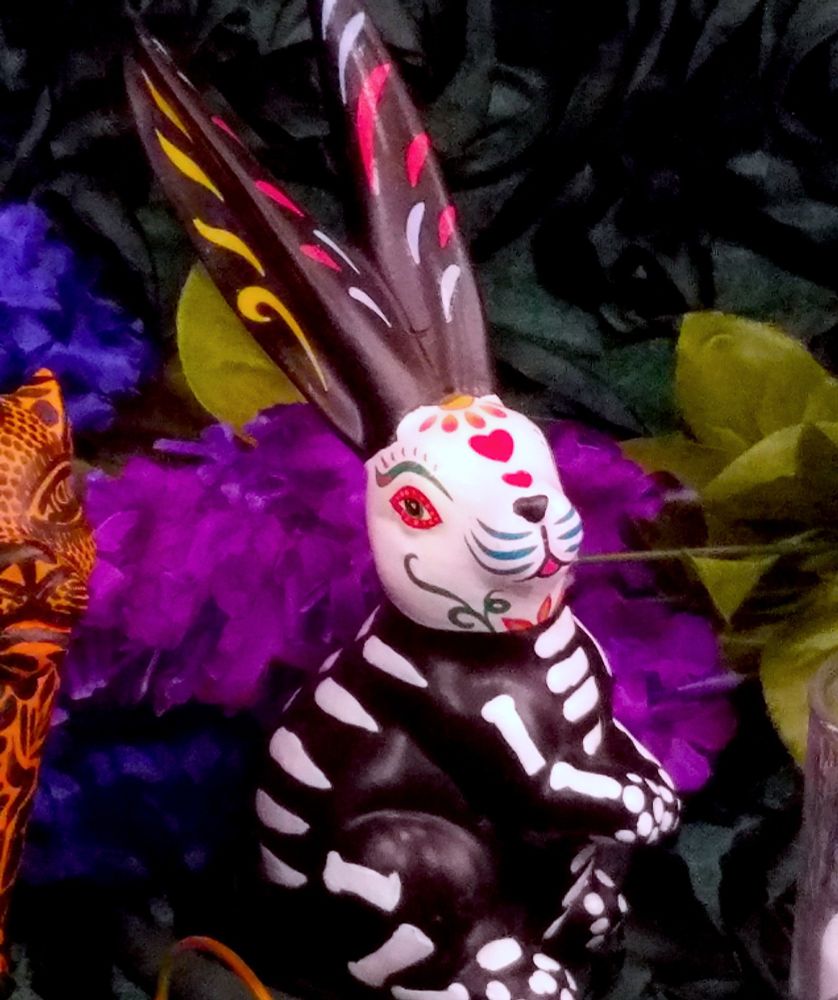 A handpainted black and white rabbit adorned with bones, hearts, and flowers sitting on a family altar for Día de Los Muertos. 
(photo taken by Kambriel)