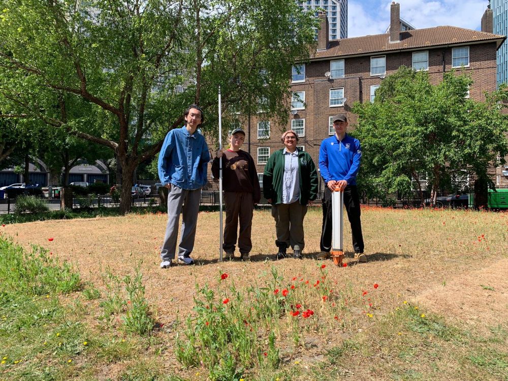 Four students post with surveying equipment on top of one of the sunken second world war bunkers in Elephant and Castle at the Rockingham Estate.