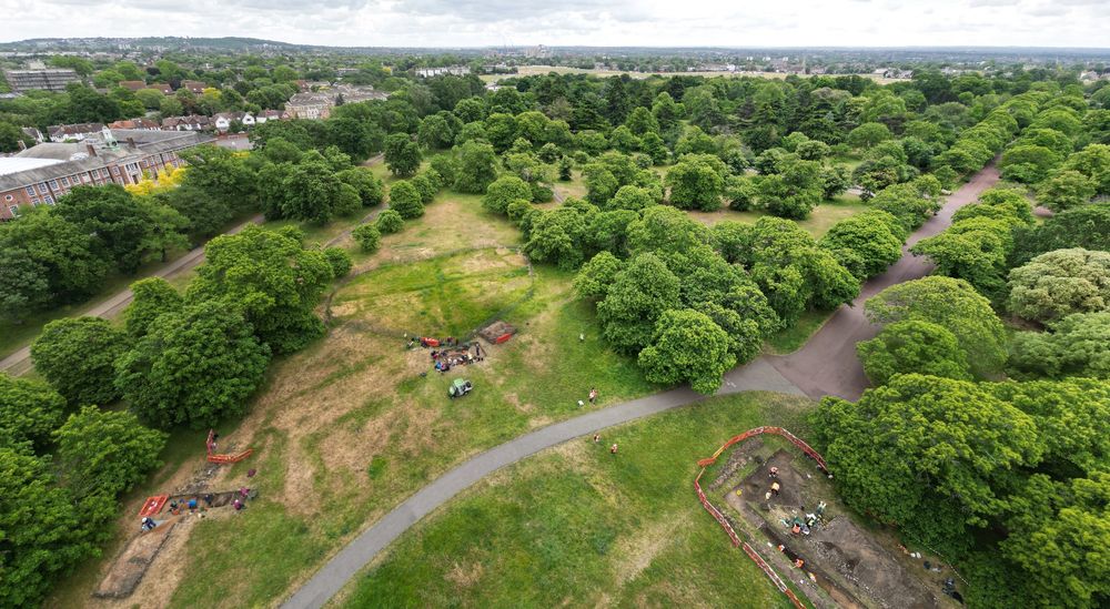 Greenwich Archaeology Project from above looking South towards Kent.  The green park and trees take up the majority of the image, with Blackheath in the background. The trenches and workers can be seen in the lower middle half of the image. Photo by Pete Barry.