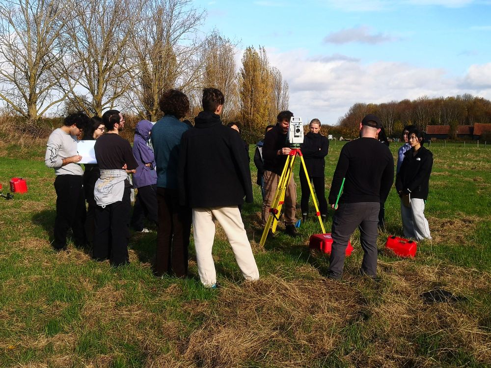 A group of students stand in a field in Hertfordshire with a total station and blue skies overhead.  Photo by Dr Kris Lockyear. 