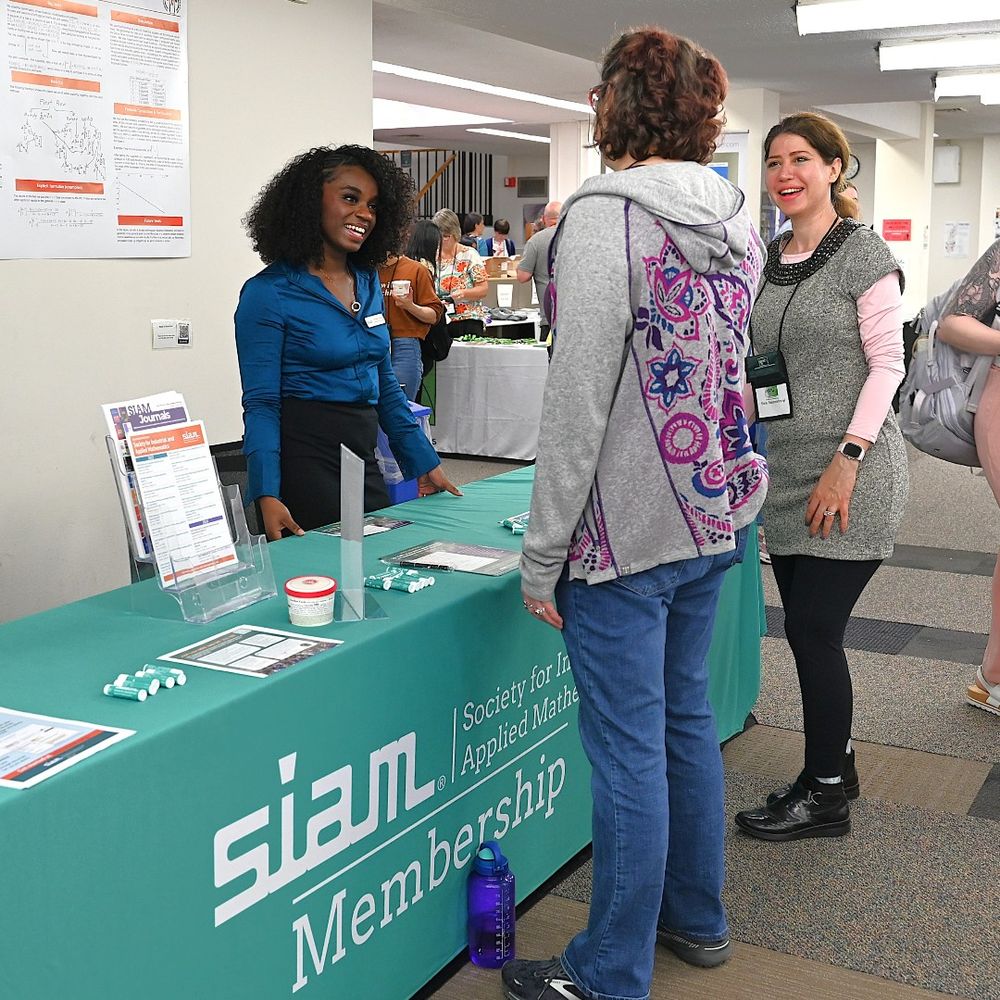 Photo of SIAM booth with SIAM representative talking to two symposium participants. 